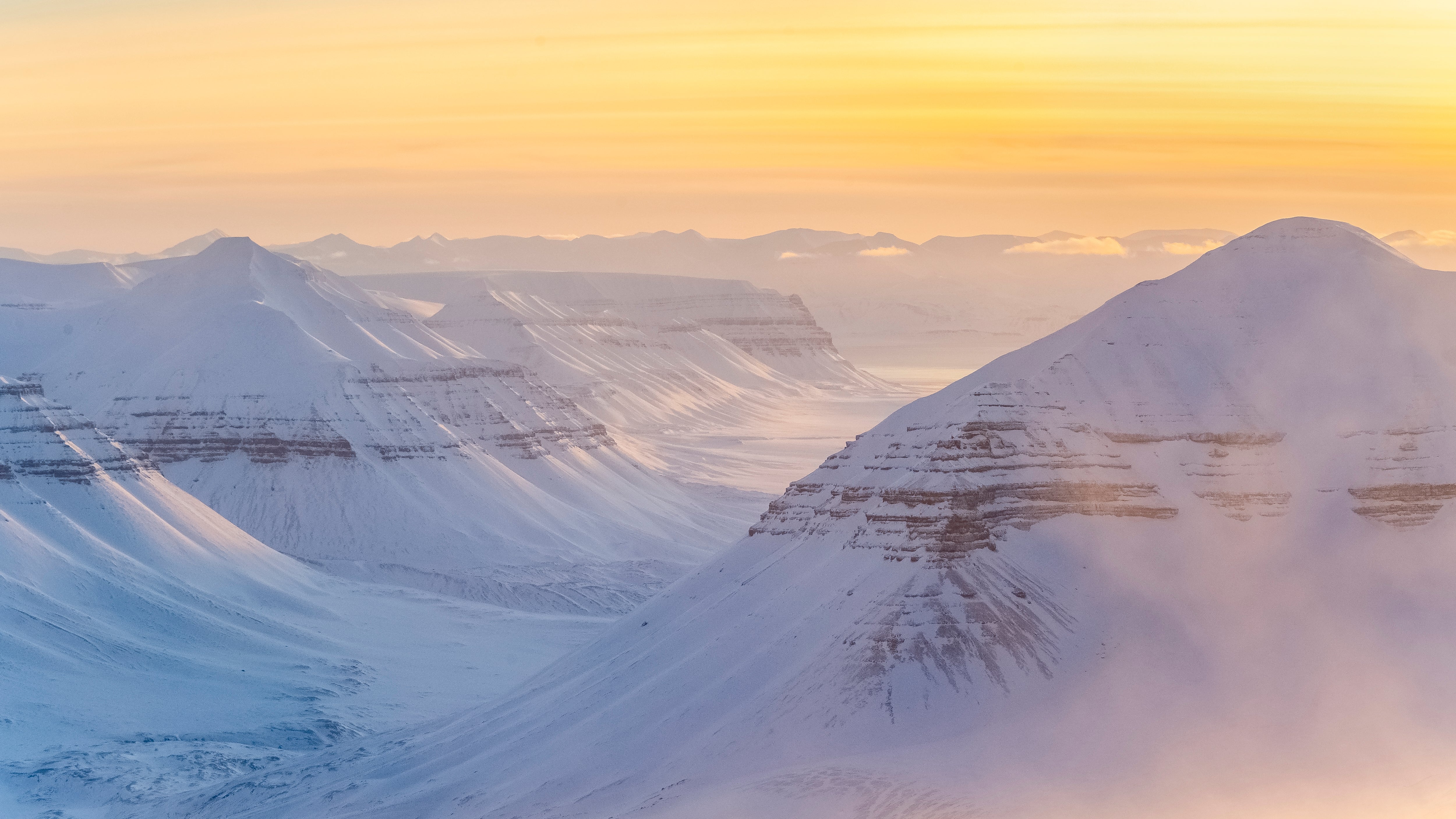 Snødekte fjelltopper i gyllen vinterdis, rekke bak rekke mot horisonten