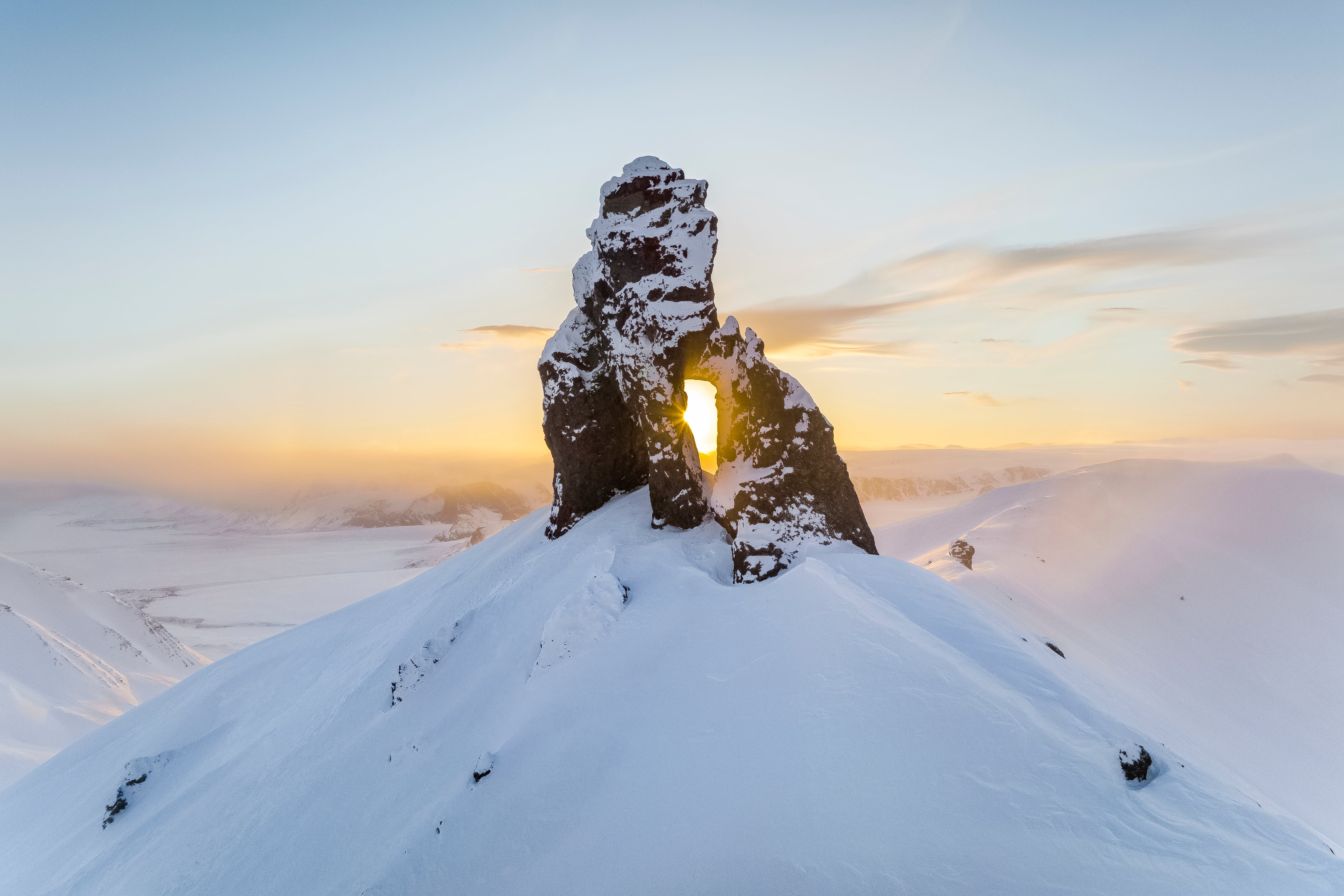 Sol som står gjennom en åpning i en klippeformasjon på en snødekt topp